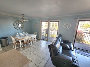 Uma sala de jantar com mesa e cadeiras, um sofá de couro preto e vista para a varanda externa.