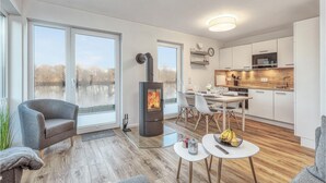 Un salon moderne doté d’une cheminée, d’un coin repas et d’une cuisine avec un plancher en bois et des armoires blanches.