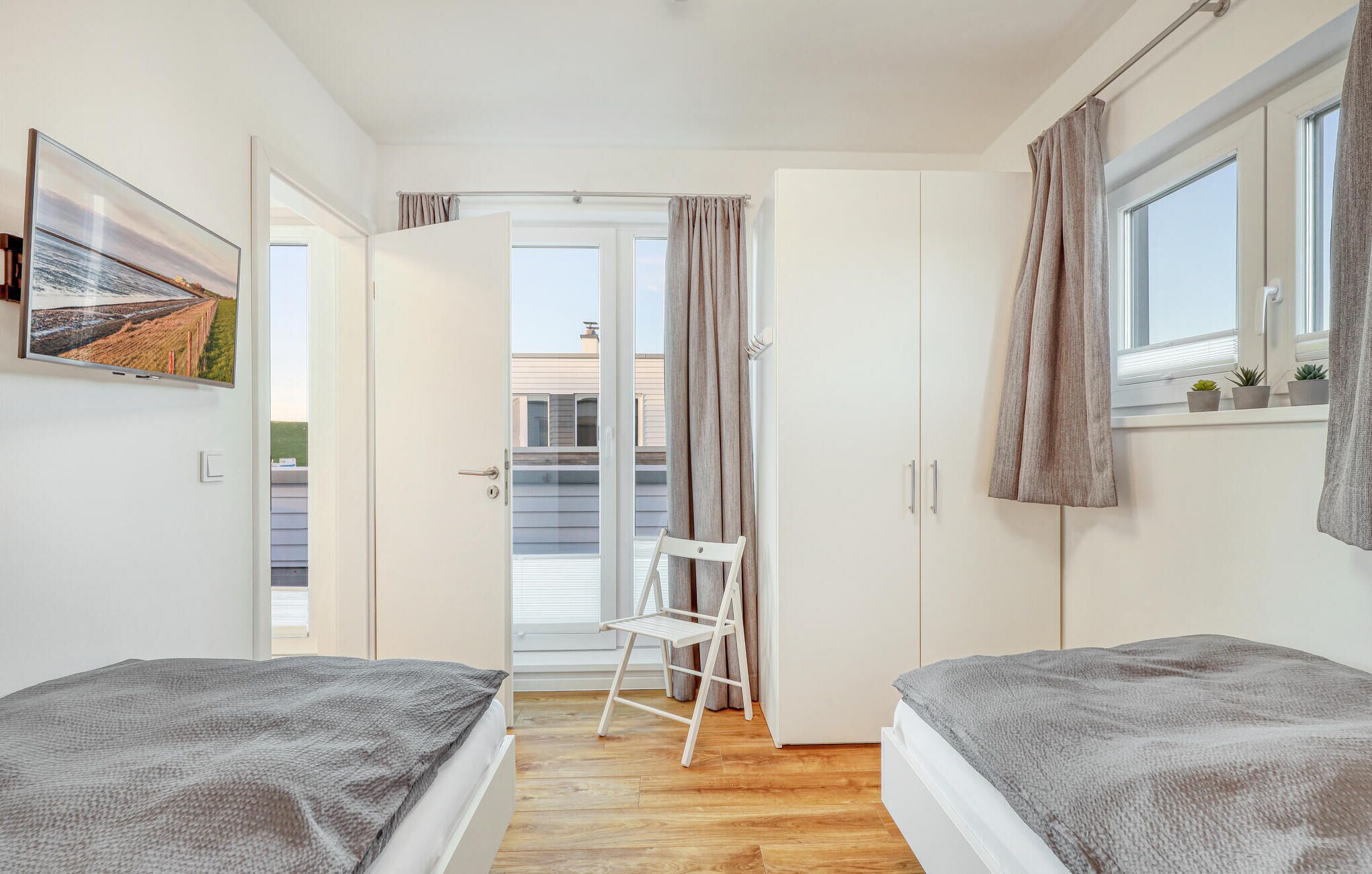 Un dormitorio con dos camas, una silla, una puerta que da a un balcón y una ventana con cortinas.