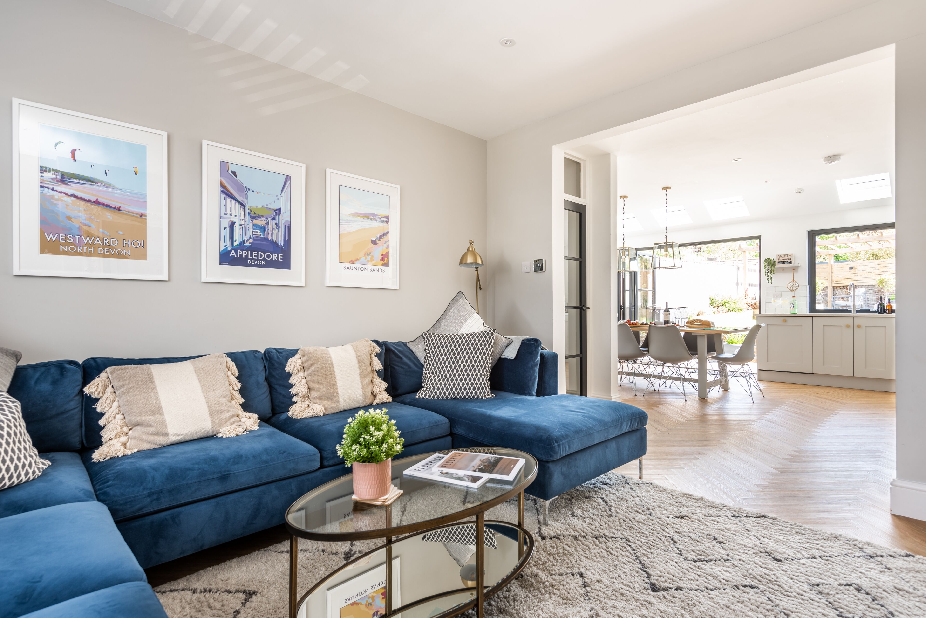 A modern living room with a blue sofa, a glass coffee table, and framed pictures on the wall.