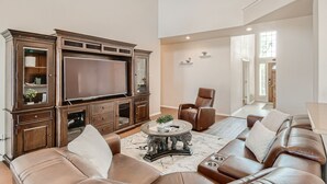 A spacious living room with a large flat-screen TV, leather sofas, a coffee table, and a built-in entertainment unit. - Home with private pool rents for longer term stay (Cedar Park)