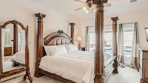 A spacious bedroom with a large bed, ornate wooden furniture, and a view of a pool. - Home with private pool rents for longer term stay (Cedar Park)