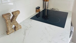 A kitchen with a black induction cooktop, white marble countertop, and wooden letter-shaped towel holders.