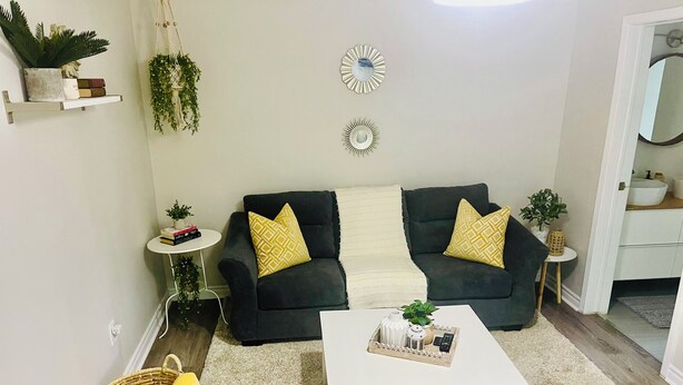 A living room with a dark sofa, two patterned pillows, a white coffee table, and a small side table with a plant.