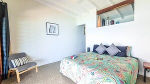 Ein Schlafzimmer mit einem Bett, einem Sessel, einem gerahmten Bild an der Wand und einem Spiegel über dem Bett.