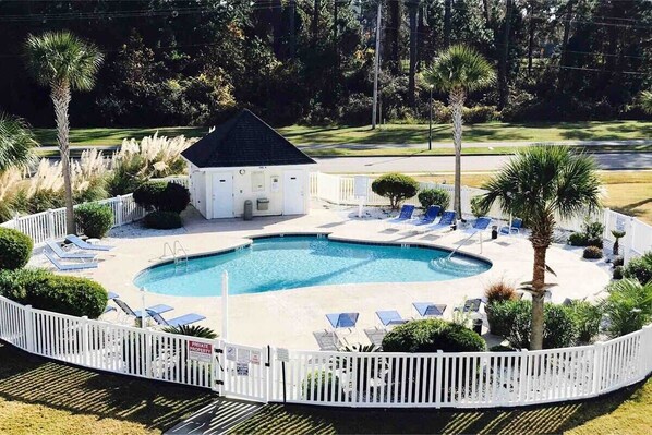 Relax by the pool surrounded by lush landscaping and a white picket fence.