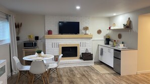 A modern kitchen with a white brick fireplace, a dining area with white chairs, and a microwave. - The Tranquil sun room (St. Catharines)