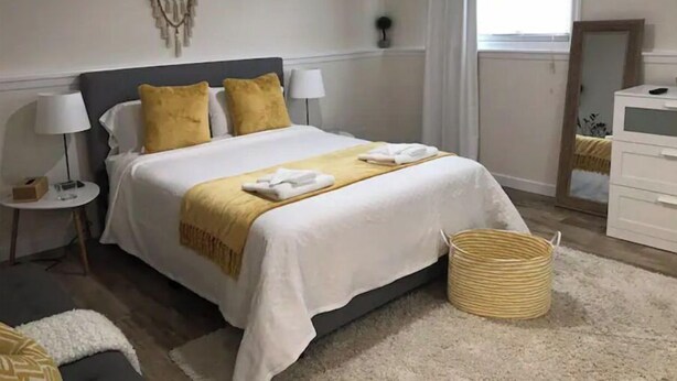 A hotel room with a bed, two bedside tables, a mirror, a window with curtains, and a small plant. - The Tranquil sun room (St. Catharines)