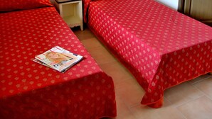 A small room with two single beds, a nightstand with a lamp, and a wooden door. - Appartement avec Parking Gratuit ! (Barjac)