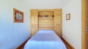 A single bed in a room with wooden paneling, a framed picture on the wall, and a small shelf with items. - 1 RC Gentianes - (Megève)