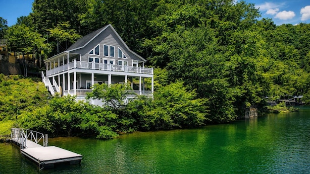 Una casa con un muelle que se adentra en un lago, rodeada de abundante vegetación.