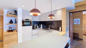 Une cuisine moderne dotée d’un îlot central, de luminaires suspendus et de meubles de rangement en bois.