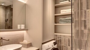 Une salle de bain moderne avec un grand miroir, un lavabo rond, un lave-linge encastré et une cabine de douche en verre.