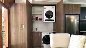 Una cocina compacta con lavadora y secadora integradas, armarios de madera y un refrigerador moderno.