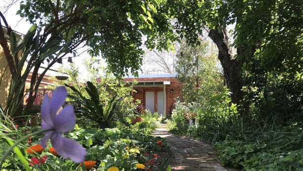 Un sendero en un jardín que conduce a un edificio con fachada de ladrillo y una puerta roja.