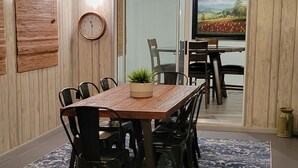 Un coin repas avec une table en bois, des chaises noires, un tapis bleu à motifs, une horloge et un téléviseur fixé au mur.