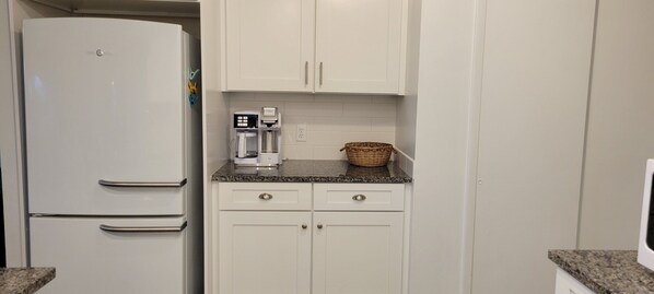 Una cocina compacta con armarios blancos, una cafetera y una cesta en la encimera.