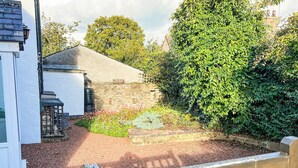 A courtyard with a stone wall, a wooden fence, and a variety of plants. - A cosy character 18th century cottage with enclosed garden close to Ullswater. (Stainton, near Penrith)