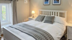A neatly made bed with a white headboard, two bedside tables with lamps, and a window with curtains. - A cosy character 18th century cottage with enclosed garden close to Ullswater. (Stainton, near Penrith)