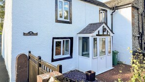 A white cottage with a small porch, a wooden gate, and a sign reading "Smithy Cottage." - A cosy character 18th century cottage with enclosed garden close to Ullswater. (Stainton, near Penrith)