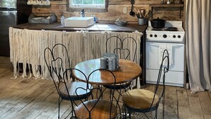 A rustic kitchen with wooden walls, a stove, and a table with chairs. - Fern Hollow Treehouse, rustic escape cozy romantic (Tishomingo)