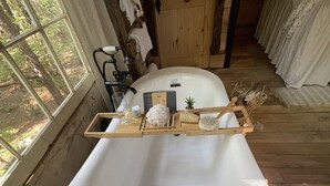 A bathtub with a wooden tray holding toiletries, a towel rack, and a small potted plant. - Fern Hollow Treehouse, rustic escape cozy romantic (Tishomingo)