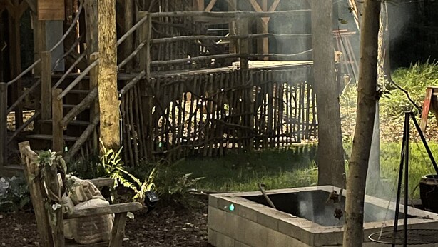 A rustic wooden cabin with a balcony, surrounded by trees and a fire pit area. - Fern Hollow Treehouse, rustic escape cozy romantic (Tishomingo)