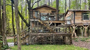 A treehouse with multiple levels, wooden railings, and a grassy area around it. - Fern Hollow Treehouse, rustic escape cozy romantic (Tishomingo)