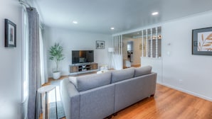 A modern living room with a grey sofa, a flat-screen TV, a potted plant, and a staircase leading to another level. - Charming  updated home in Midtown (Tulsa)