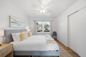 A bedroom with a bed, bedside tables, a chair, a window, and a ceiling fan.