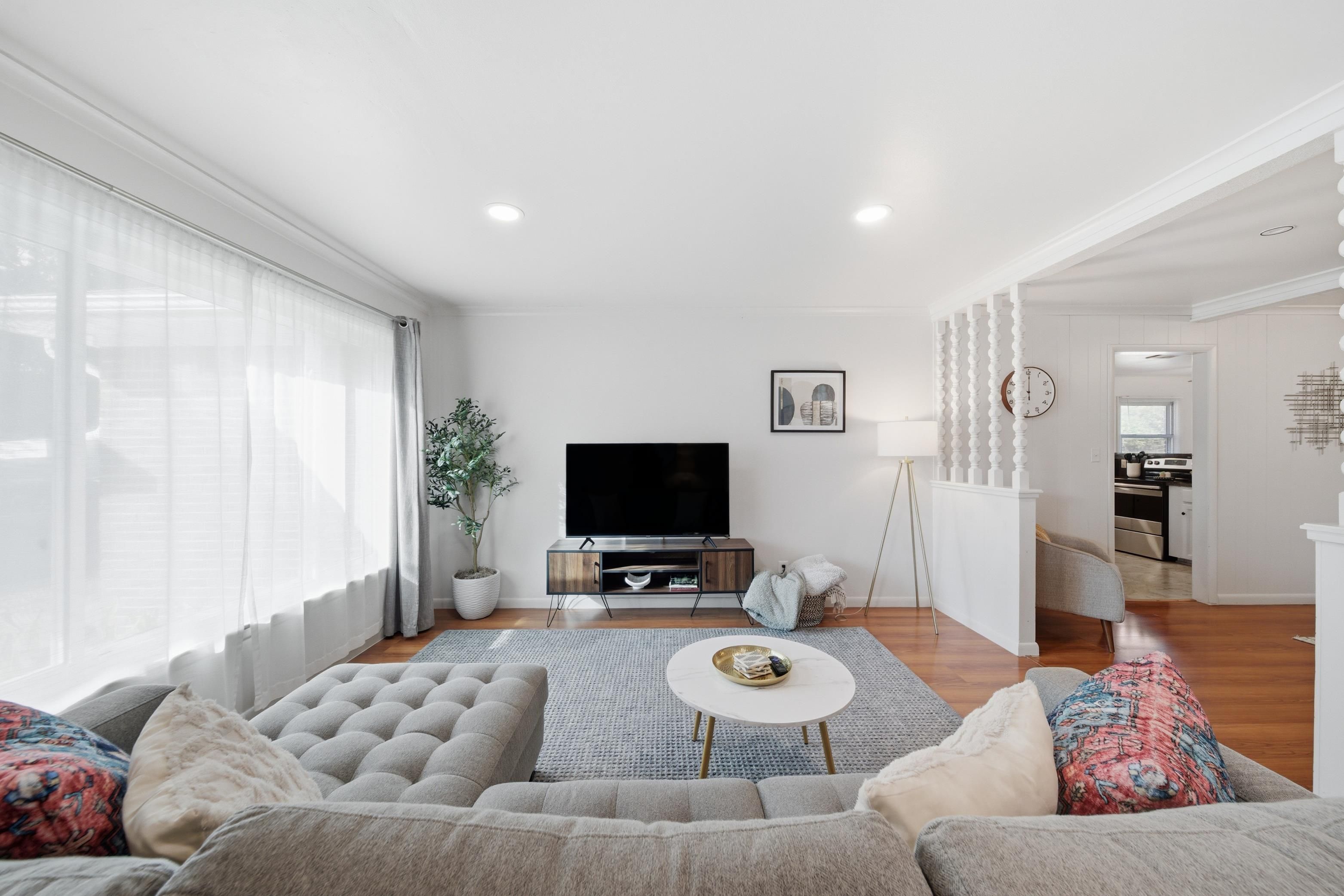 A modern living room with a large sofa, a flat-screen TV, and a dining area with a kitchen in the background.