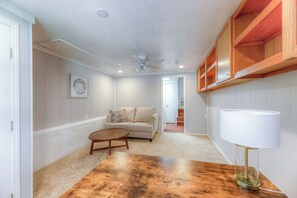 A room with a wooden table, a sofa, a ceiling fan, and built-in wooden shelves. - Charming mid century modern home in Midtown (Tulsa)