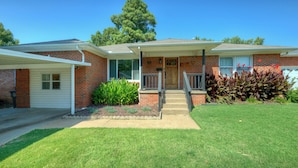 A two-story brick house with a front porch, a garage, and a well-maintained lawn. - Charming  updated home in Midtown (Tulsa)