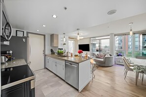 A modern kitchen with a central island, built-in appliances, and a dining area with a table and chairs. - The Pond - The Full Package (Vancouver)
