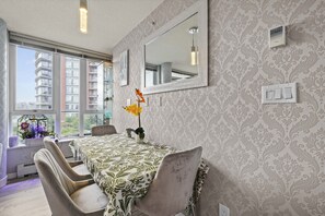 A modern dining area with a patterned tablecloth, a large mirror, and a view of a building through large windows. - The Pond - The Full Package (Vancouver)