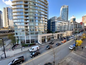 A modern urban street with high-rise buildings, a multi-story parking garage, and a busy road with vehicles.