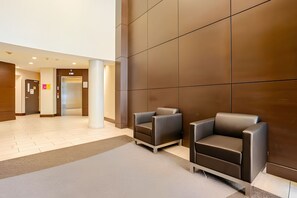 A modern lobby with two leather chairs, a reception desk, and a digital elevator display. - The Pond - The Full Package (Vancouver)