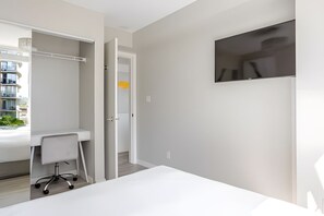 A modern bedroom with a white desk, chair, and a TV mounted on the wall.