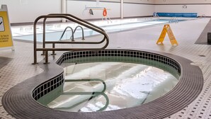 An indoor swimming pool with a tiled floor, a metal handrail, and a clear ceiling with visible ductwork.