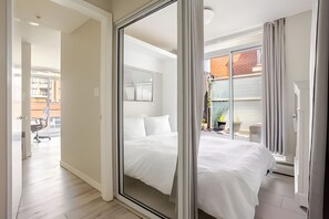 A modern bedroom with a large bed, a sliding glass door leading to a balcony, and a view of a building outside. - The Pond - The Full Package (Vancouver)
