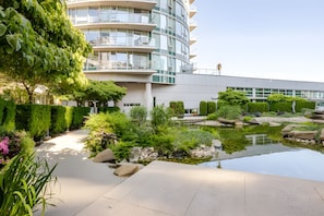 A modern building with a curved facade, a landscaped garden with a pond, and a clear sky.