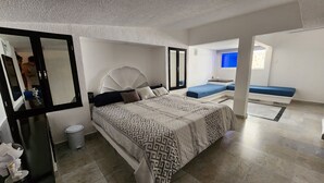 Un dormitorio con cama, espejo, un espacio para sentarse y baño.