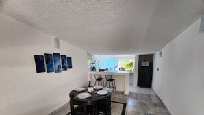Comedor con mesa lista para cuatro, cocina al fondo y vista al exterior.