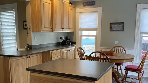 A kitchen with wooden cabinets, a black countertop, and a dining area with a table and chairs. - Renovated Victorian in 'Americas Coolest Small Town' (Hammondsport)