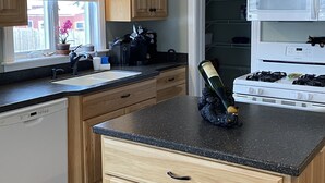 A kitchen with wooden cabinets, a black countertop, a sink, a dishwasher, a stove, and a microwave. - Renovated Victorian in 'Americas Coolest Small Town' (Hammondsport)