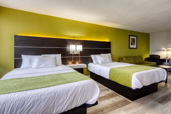 A hotel room with two beds, each with white bedding and green throw blankets, a nightstand with a lamp, and a green wall. - Hotel Weston (Marietta)
