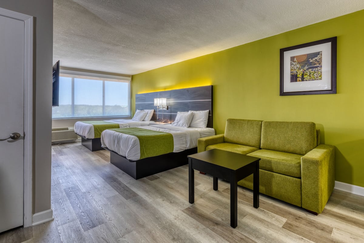 Una habitación de hotel con dos camas, un sofá verde, una mesita y un cuadro en la pared.