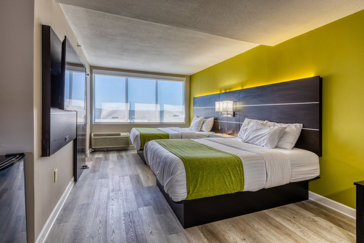 Una habitación de hotel moderna con dos camas, un ventanal grande, un televisor de pantalla plana y vistas a la ciudad.