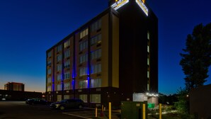 Ein mehrstöckiges Hotelgebäude mit beleuchteter Beschilderung, einem Parkplatz und einem grünen Verteilerkasten.