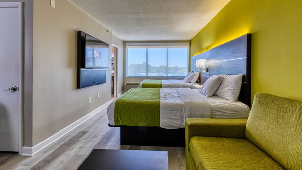 Ein Hotelzimmer mit einem großen Bett, einem grünen Sofa, einem Flachbildfernseher und einem Fenster mit Blick auf die Stadt.
